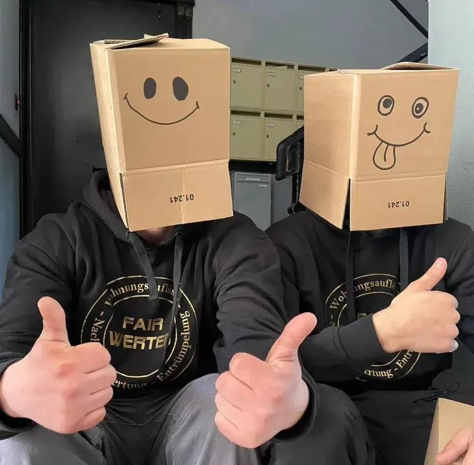 Wohnungsauflösung, hier zu sehen zwei Mitarbeiter mit lächelnden Kartons auf dem Kopf