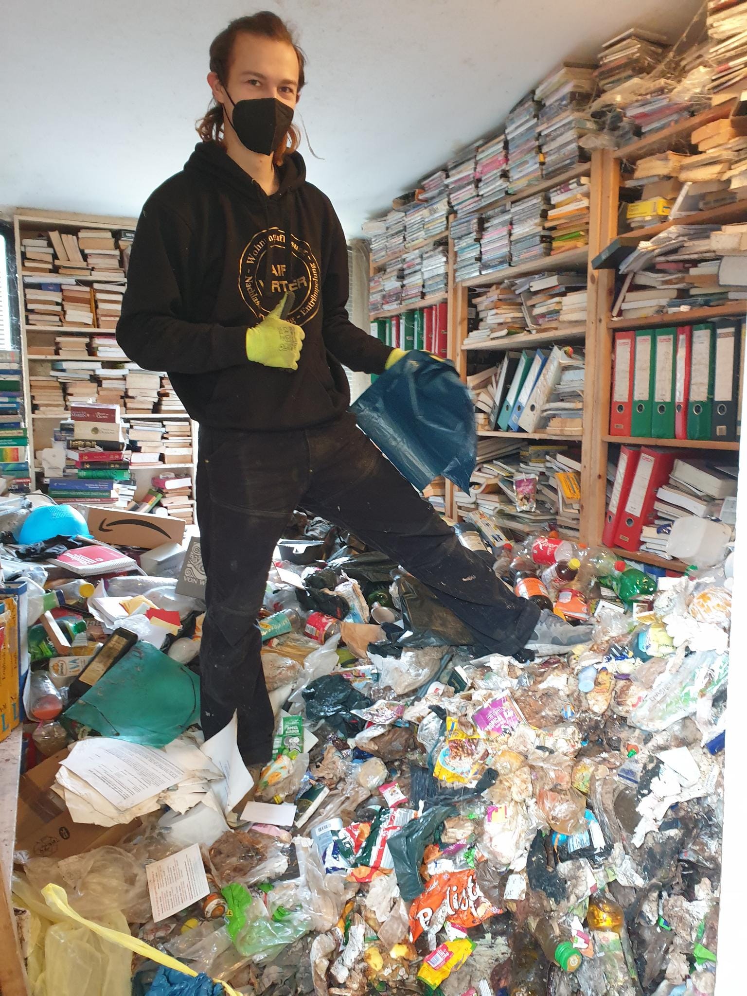Messie-Wohnung - FAIRwerter Berlin Messie-Wohnung, hier zu sehen ein Mitarbeiter in einem Zimmer voller Bücherregale und Hausmüll auf dem Boden