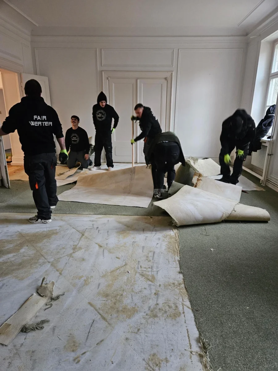 FAIRwerter_Bodenbelagsentfernung Mitarbeiter beim Entfernen von voll verklebtem Teppichboden während einer Wohnungsauflösung